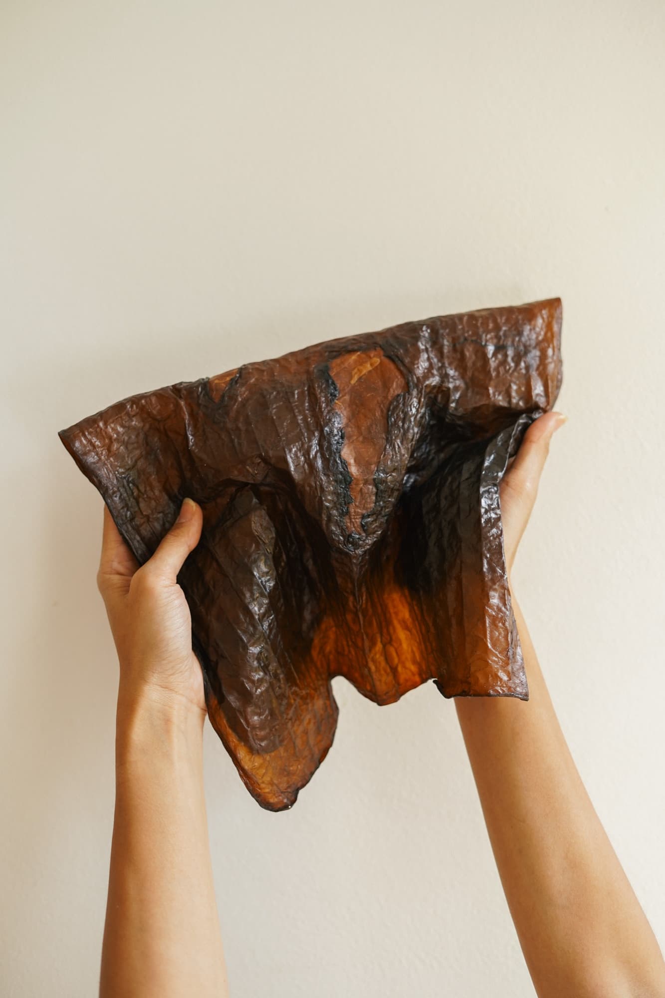 Two hands holding up a full sheet of Kombucha Bioleather against a pale wall