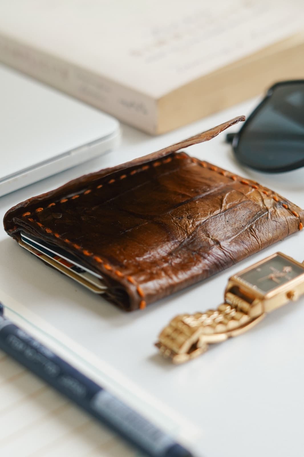 A Symbia bioleather wallet with sunglasses and a watch, flat lay