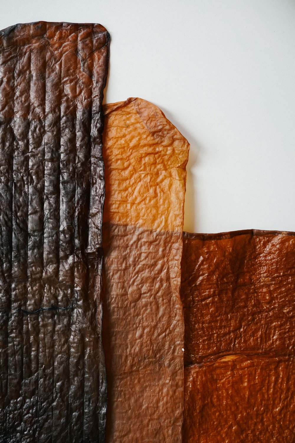 Three sheets of bioleather side by side, from pale amber through to near black